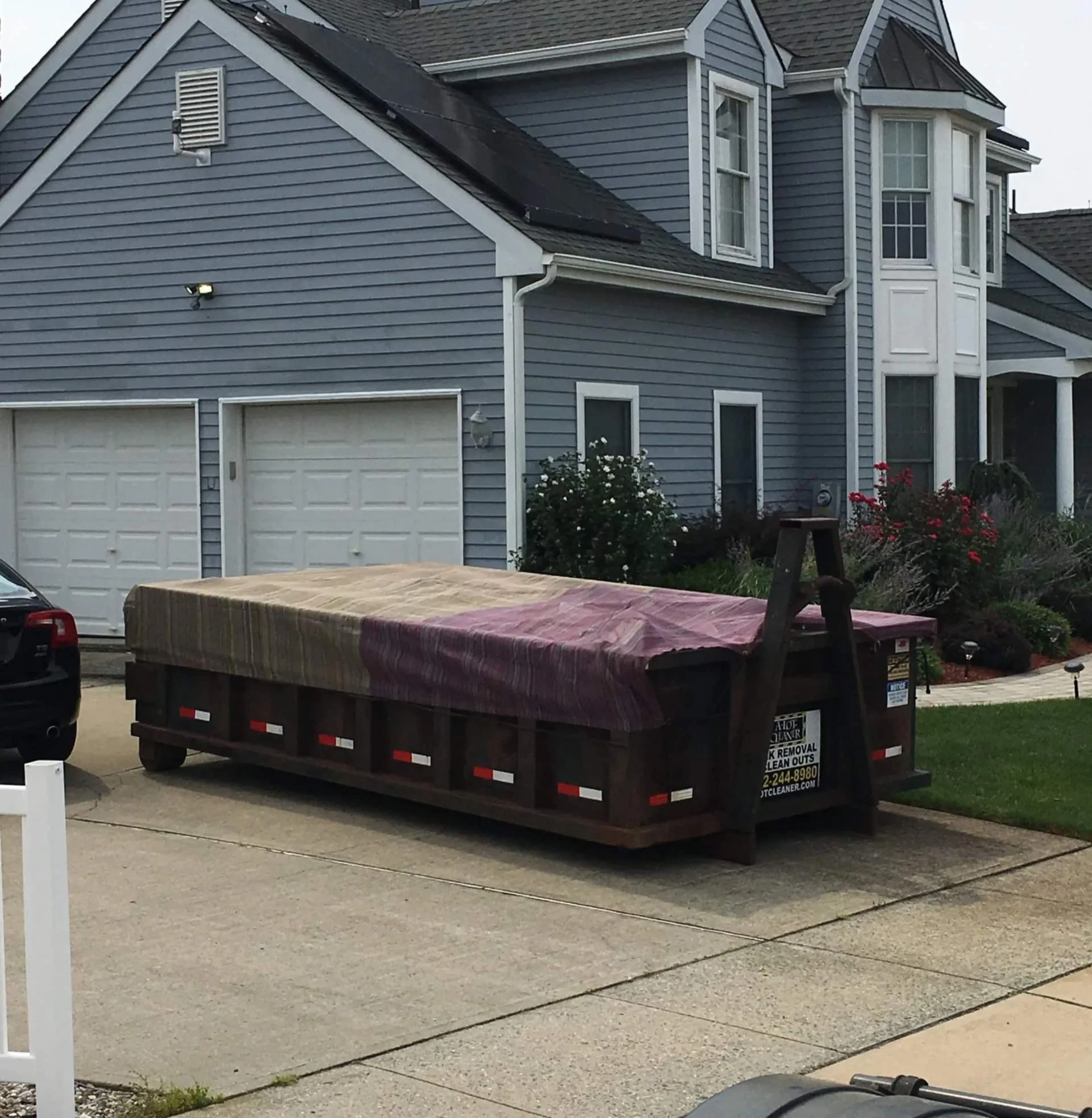 Dumpster covered with a brown and purple tarp parked on a concrete driveway